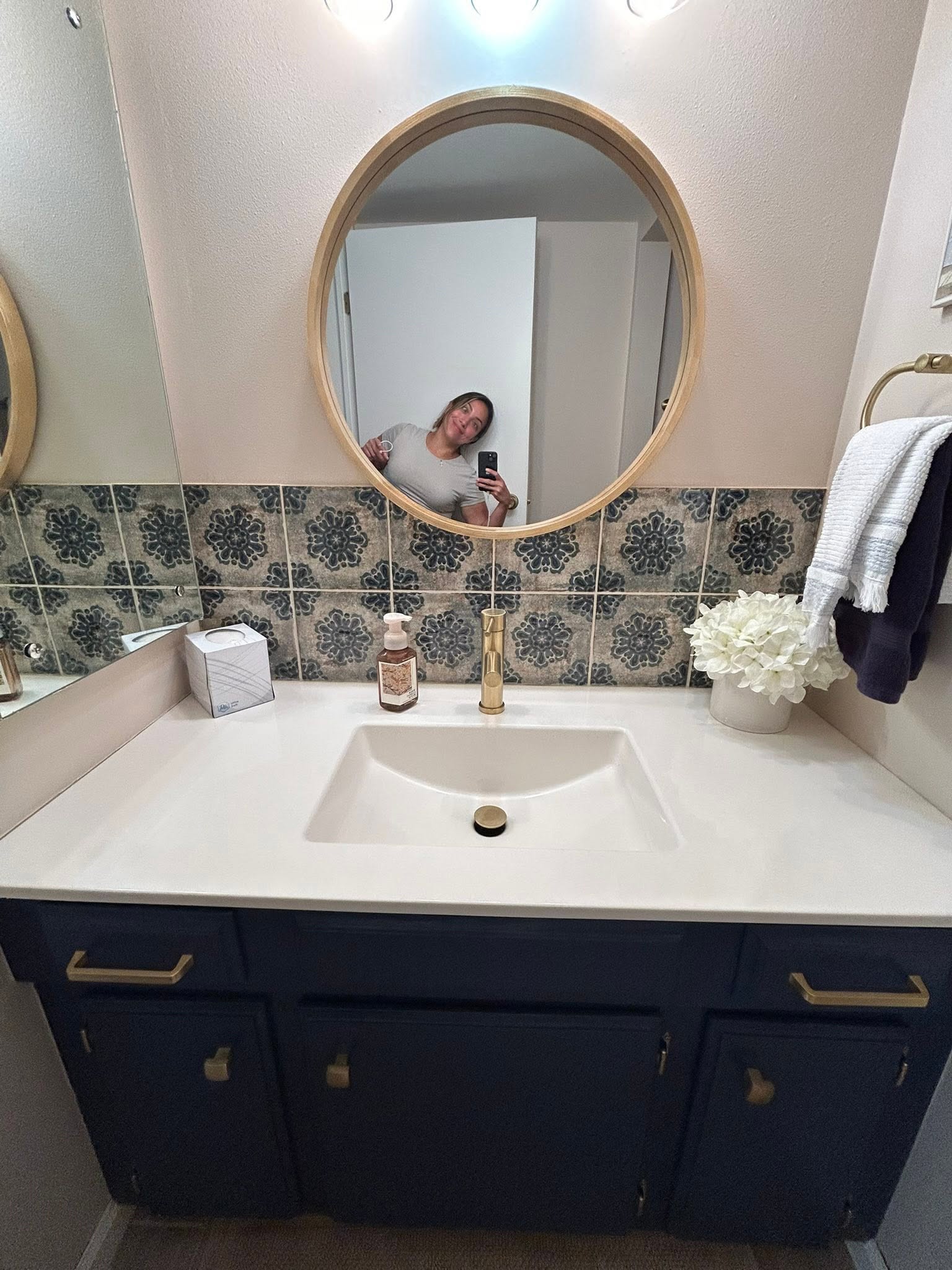 GC cleaner taking a mirror selfie beside a finished navy vanity staged with fresh towels and flowers