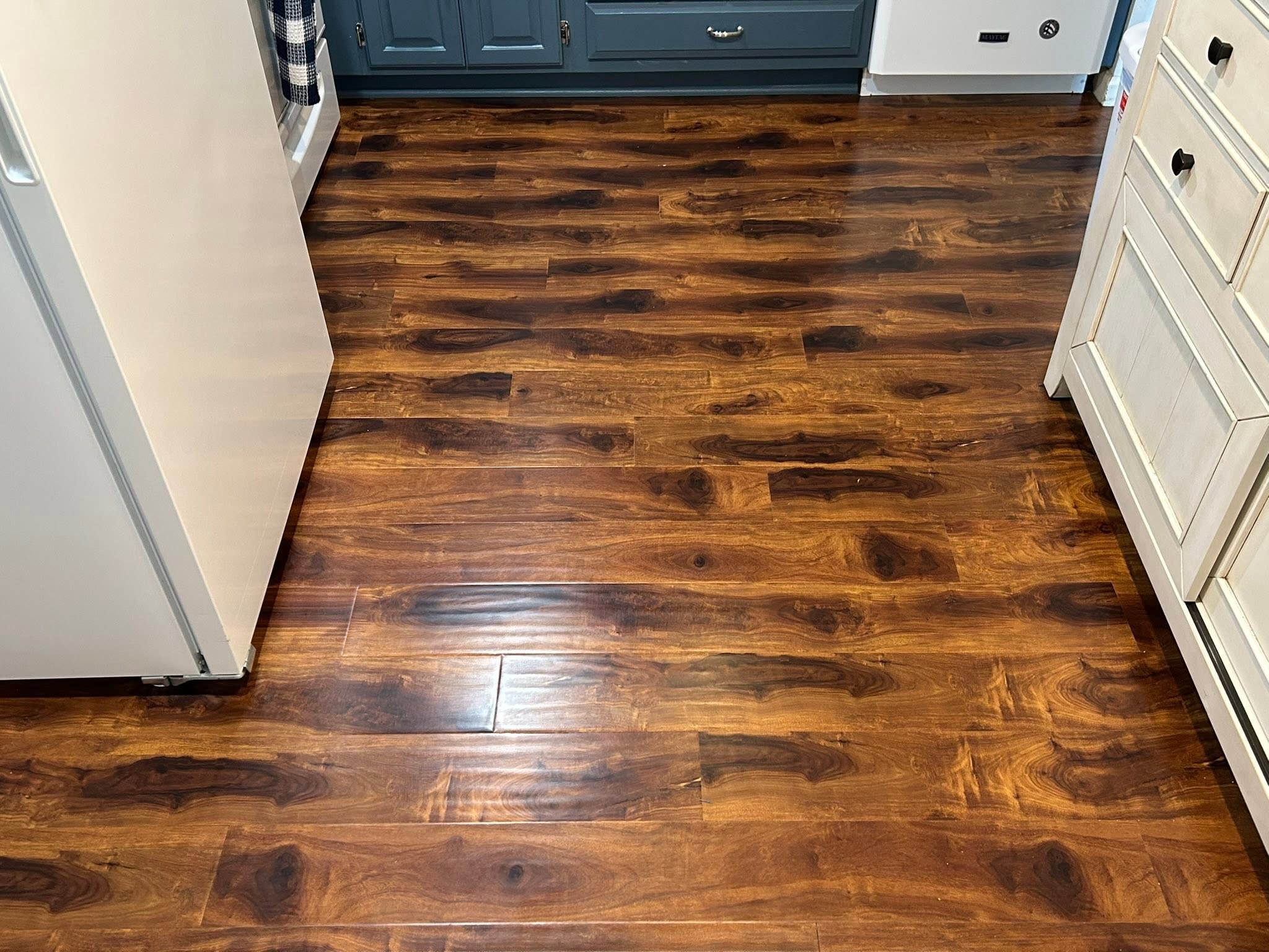 Dark hardwood kitchen floor cleaned to a shine between white and blue cabinets