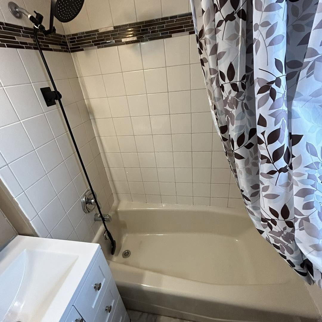 Deep-cleaned tub and shower with white square tile, a glass mosaic accent stripe, and a fresh floral curtain