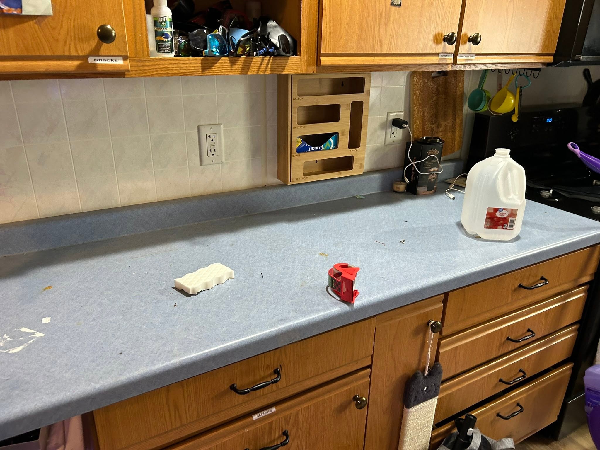 Kitchen counter before cleaning: crumbs and debris across the blue laminate, a sponge and a water jug left out