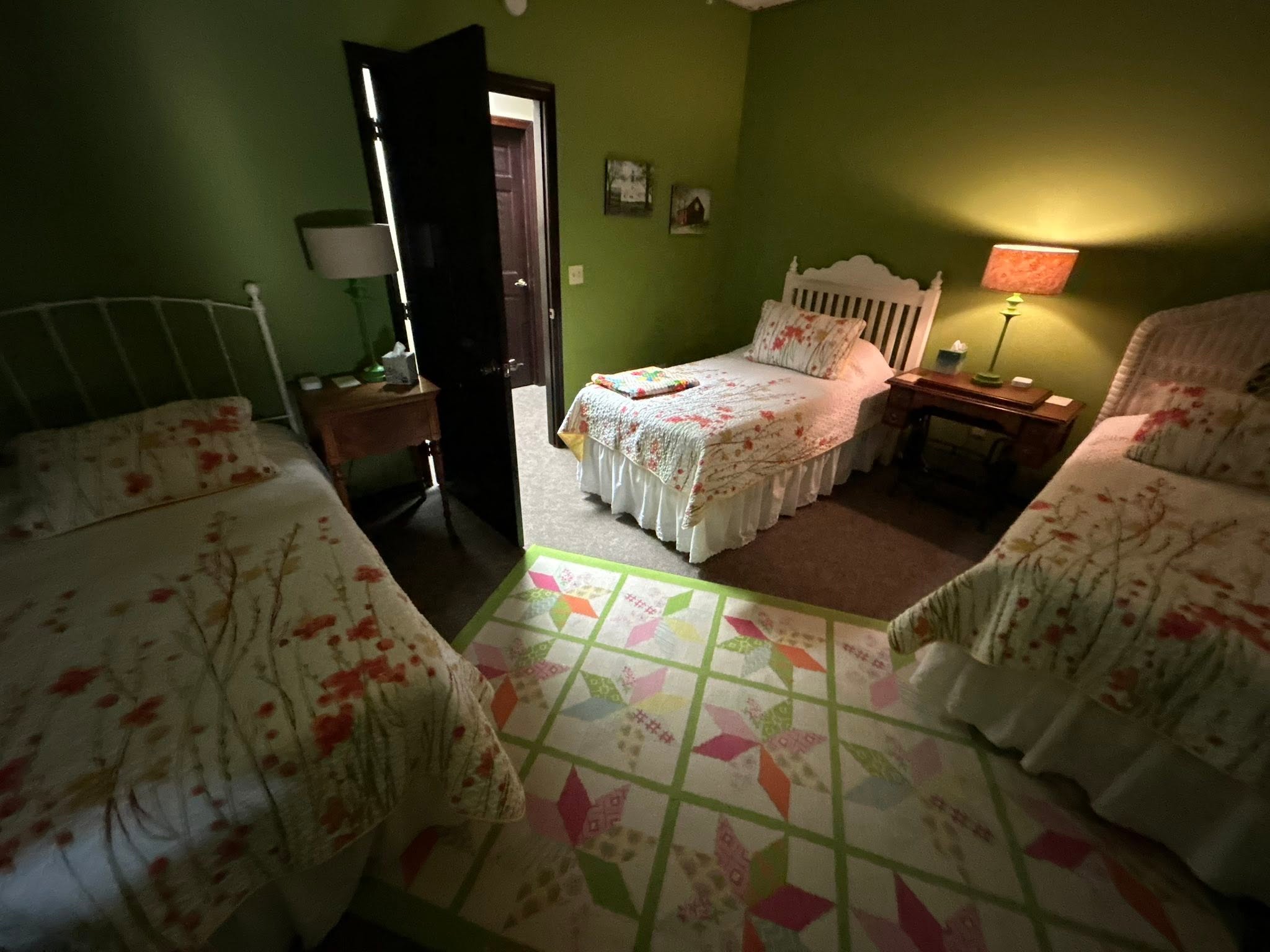 Green guest room with three quilted beds made up and a star quilt rug on the floor