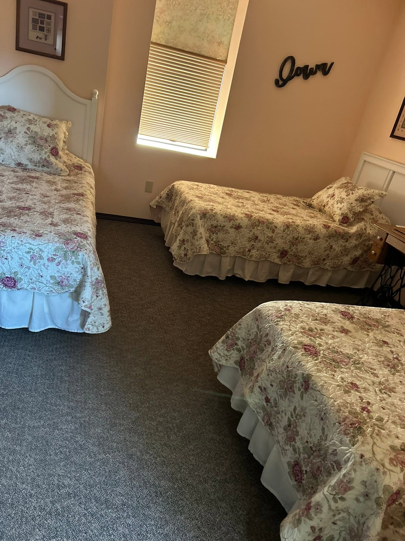 Peach guest room with three floral beds made up beside an Iowa wall sign