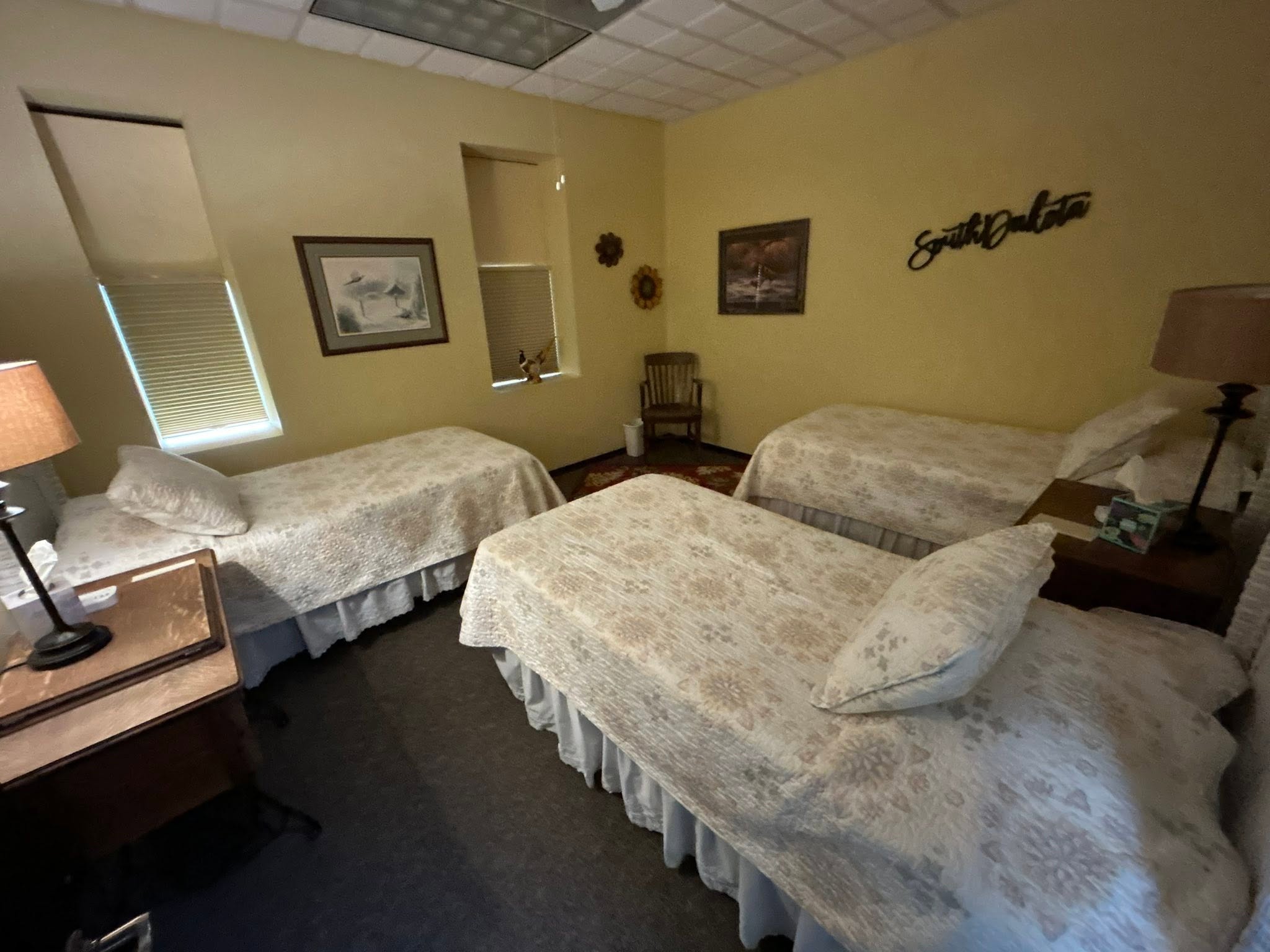Commercial guest room turned over by GC: three beds made up under a South Dakota wall sign